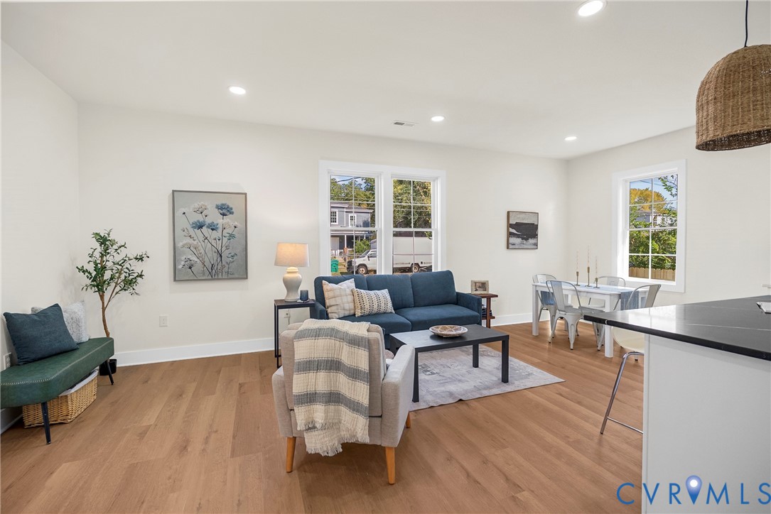 Open-concept living space featuring wood-finish flooring, recessed lighting, double-hung windows with mullions, and a kitchen island with a dark solid-surface countertop
