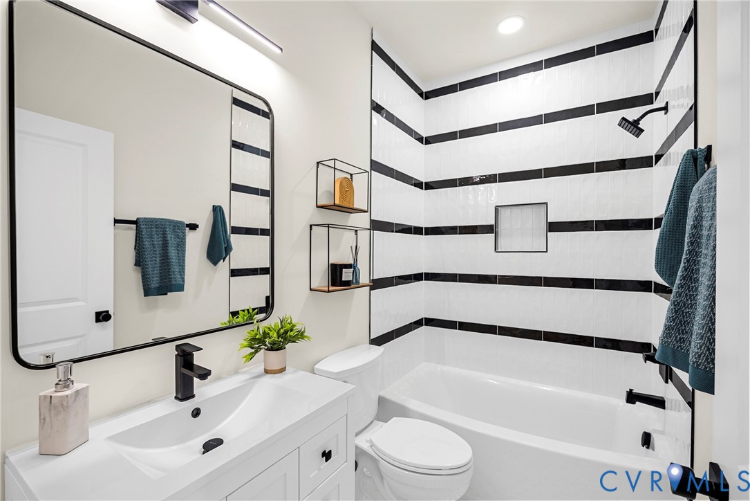Bathroom featuring a white vanity with a rectangular sink, black matte hardware, a rectangular vanity mirror with a black frame, and a tub-shower combination accented with horizontal black and white wall tile
