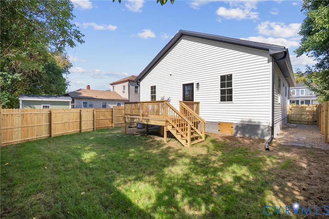 Exterior featuring vinyl siding, a wood deck with stairs, a wooden privacy fence, and a gravel side path