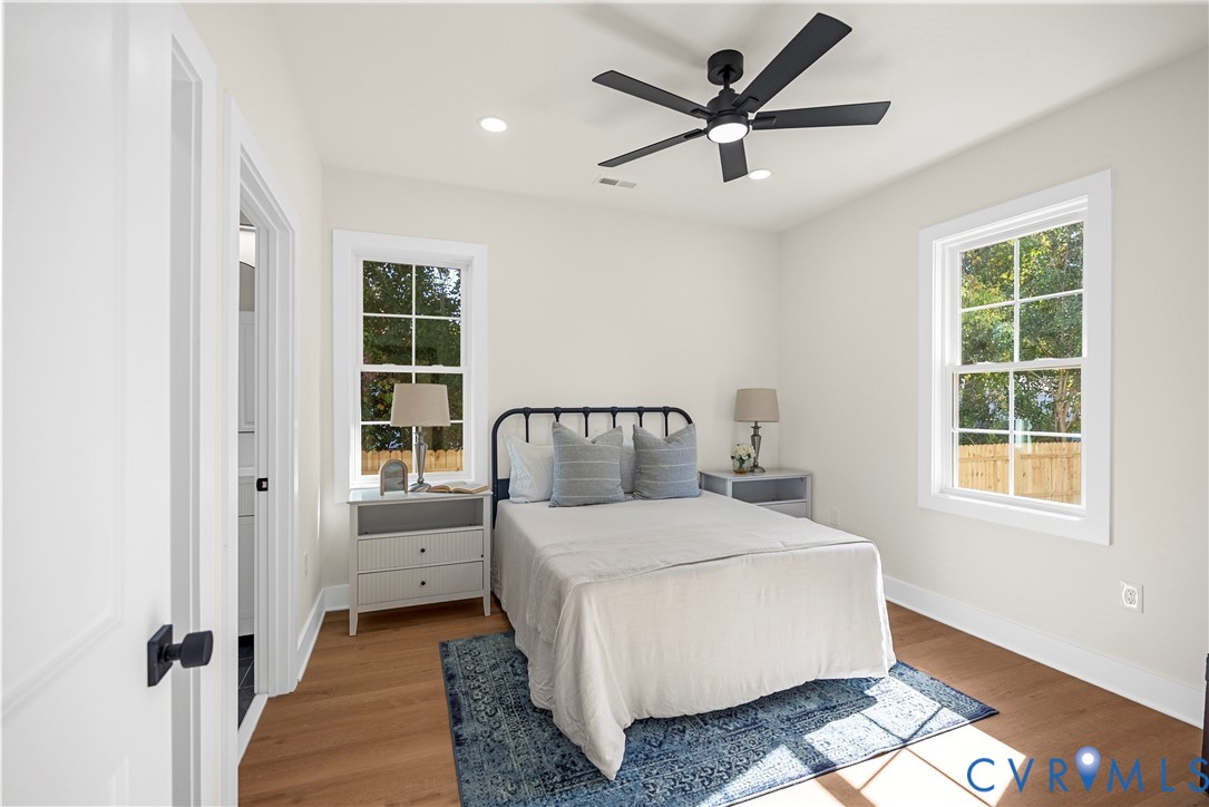 Light-filled room featuring wood-finish flooring, dual grid-pane windows, recessed lighting, and a matte black ceiling fan