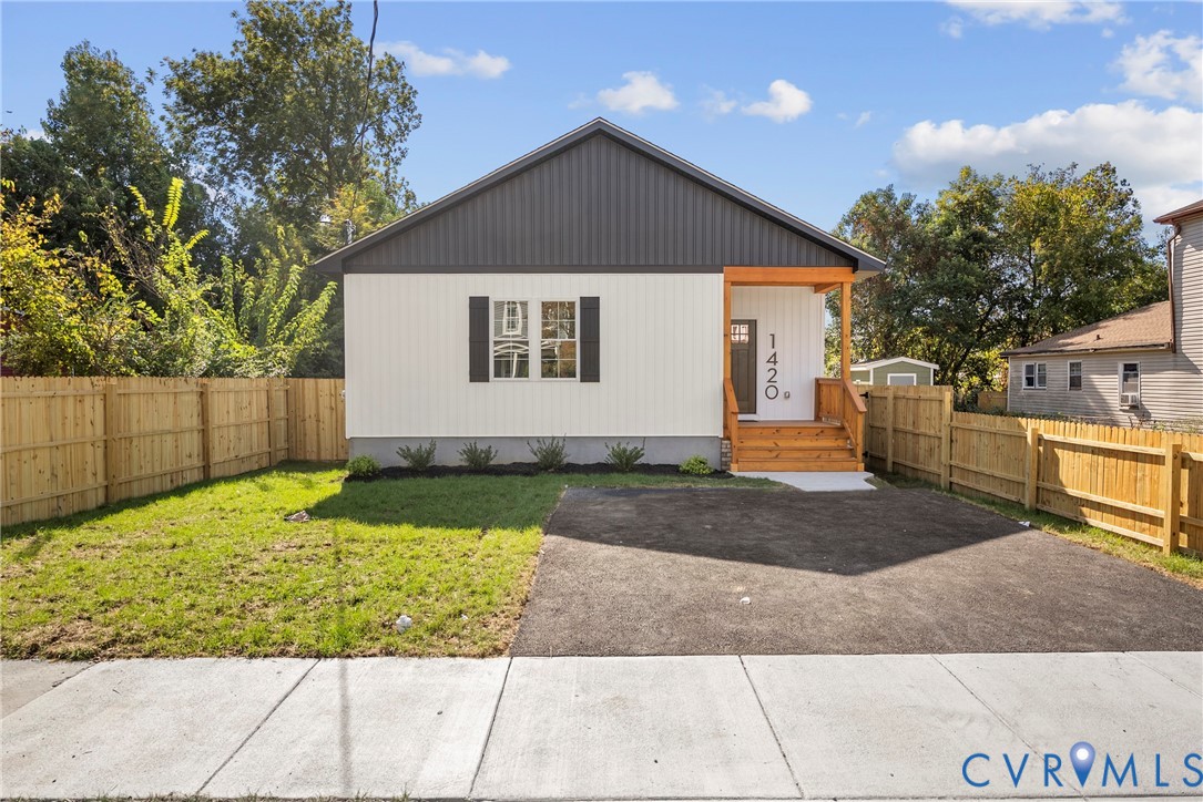 Single-story exterior featuring board-and-batten siding, a covered porch with exposed wood support beams, asphalt paved driveway, and a wood privacy fence