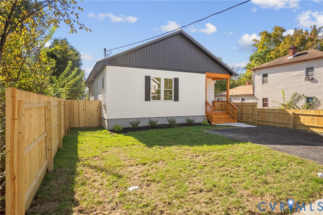 Exterior featuring dual-tone vertical siding, natural wood front porch, asphalt driveway, and perimeter wood privacy fencing