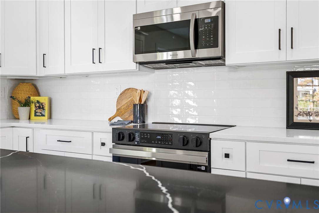 Kitchen featuring white shaker-style cabinetry, dark stone-finish island countertop, white quartz perimeter countertops, subway tile backsplash, and stainless steel appliances