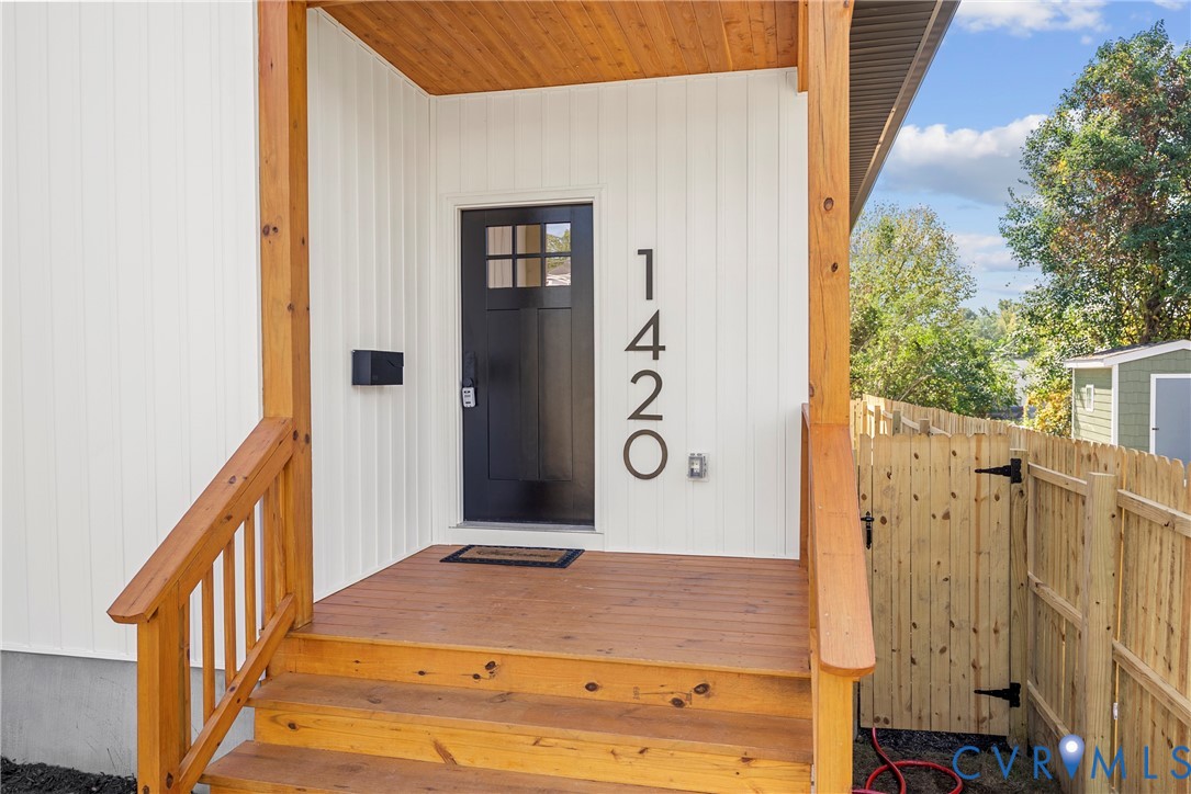 Covered front porch featuring wood-finish decking, natural wood support posts, vertical board-and-batten siding, and a dark-toned door with glass panel inserts