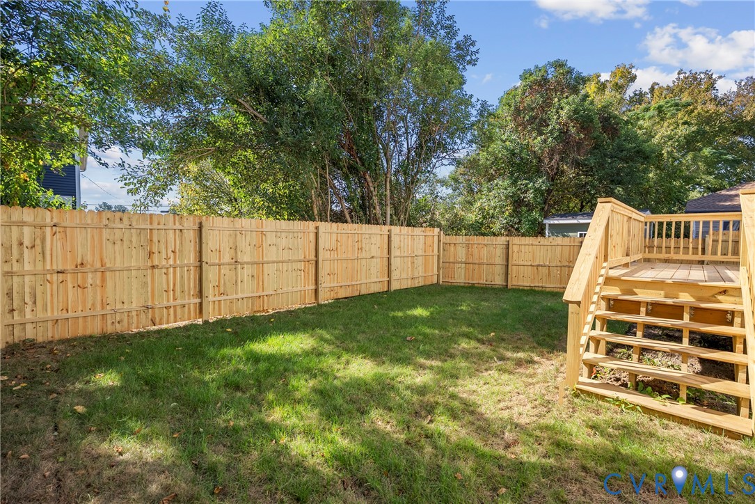 Private backyard featuring a wood-plank privacy fence, manicured lawn, and raised wooden deck with integrated steps