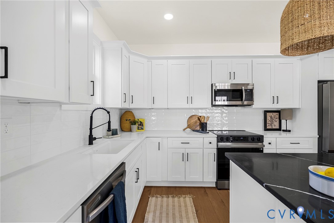 Kitchen featuring white shaker-style cabinetry, white countertops, subway tile backsplash, stainless steel appliances, and a dark-toned island countertop