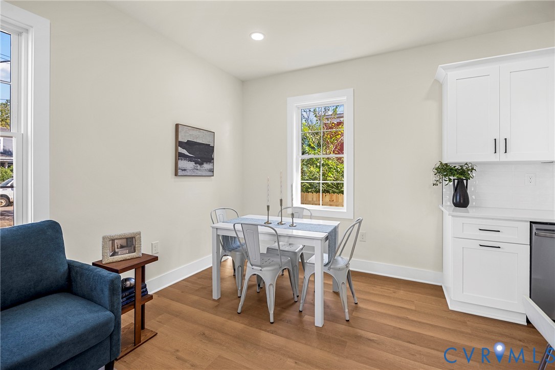 Wood-finish flooring, white shaker-style cabinetry with dark hardware, recessed lighting, and dual-pane windows