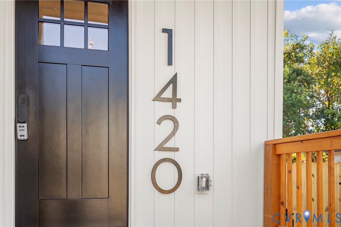 Vertical board siding, high-contrast dark entry door with multi-pane window inlay, and oversized metallic house numerals