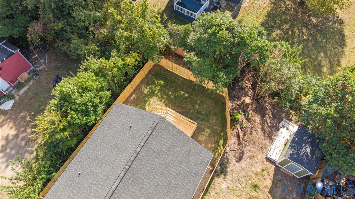 Fenced backyard featuring a wood deck, mature trees, and a detached storage structure