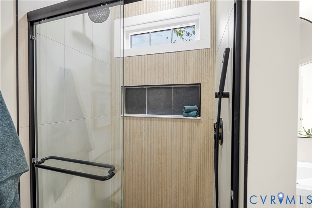 Walk-in shower featuring a frameless glass door, matte black fixtures, rainfall showerhead, integrated tiled wall niche, and textured wood-finish tiling