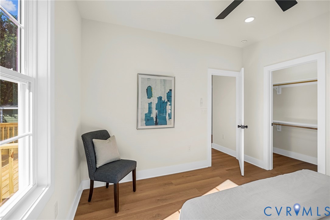 Neutral-toned walls featuring wood-finish flooring, a multi-pane window, a ceiling fan, and a walk-in closet with built-in shelving