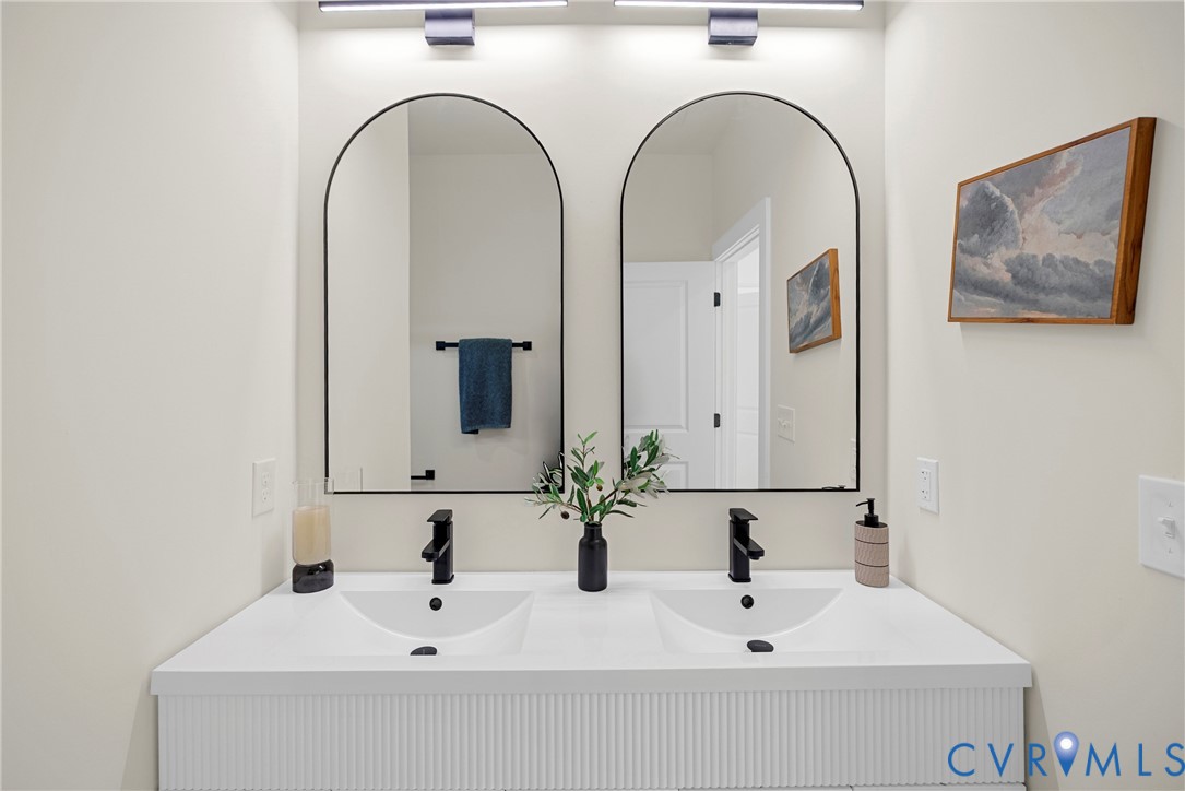 Double vanity with white integrated dual sinks, textured fluted cabinetry, matte black wall-mounted faucets, and dual arched mirrors with black frames