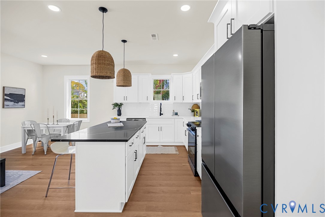 Kitchen featuring white shaker-style cabinetry, dark stone countertops, stainless steel appliances, wood-finish flooring, and dual woven pendant lights
