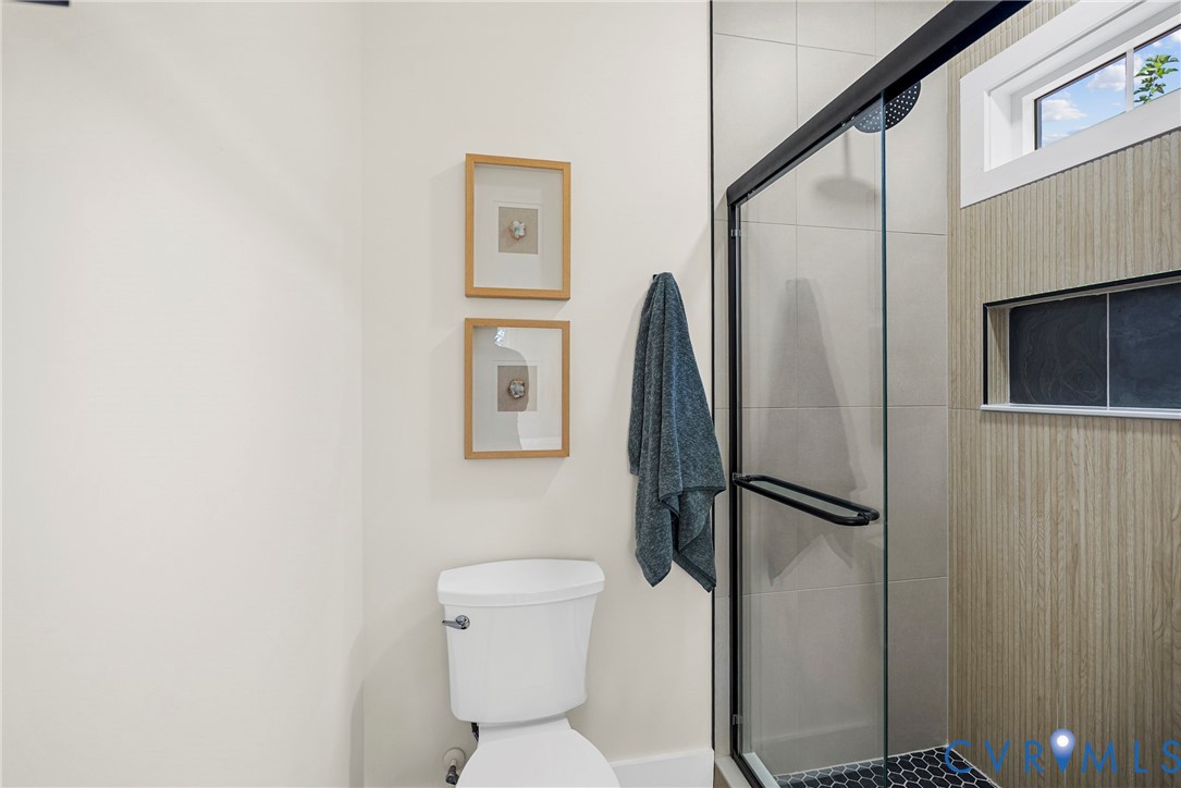 Walk-in shower with matte black fixtures, glass enclosure, large-format tile surround, recessed wall niche, and hexagon floor tile
