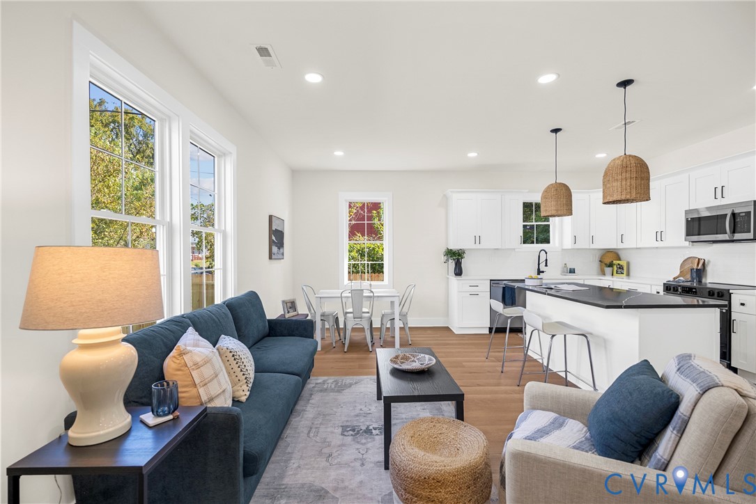 Open-concept living space featuring wood-finish flooring, recessed lighting, white cabinetry, a center island with a dark countertop, and large windows