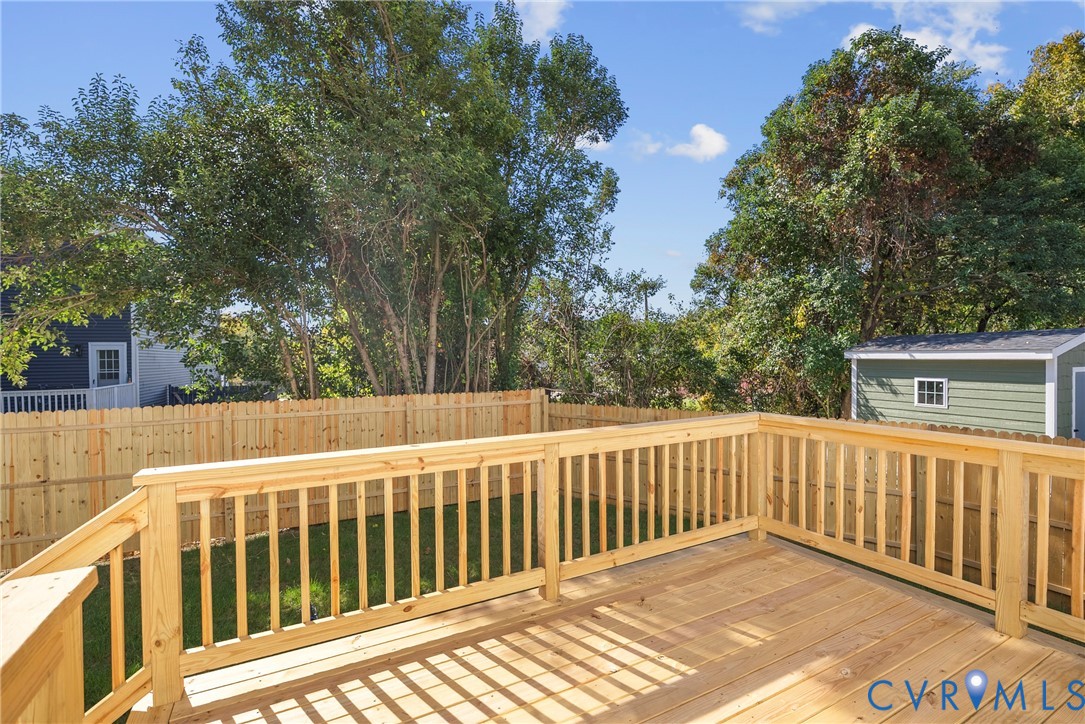 Elevated wood deck featuring vertical baluster railings, wood fencing, and a detached storage structure