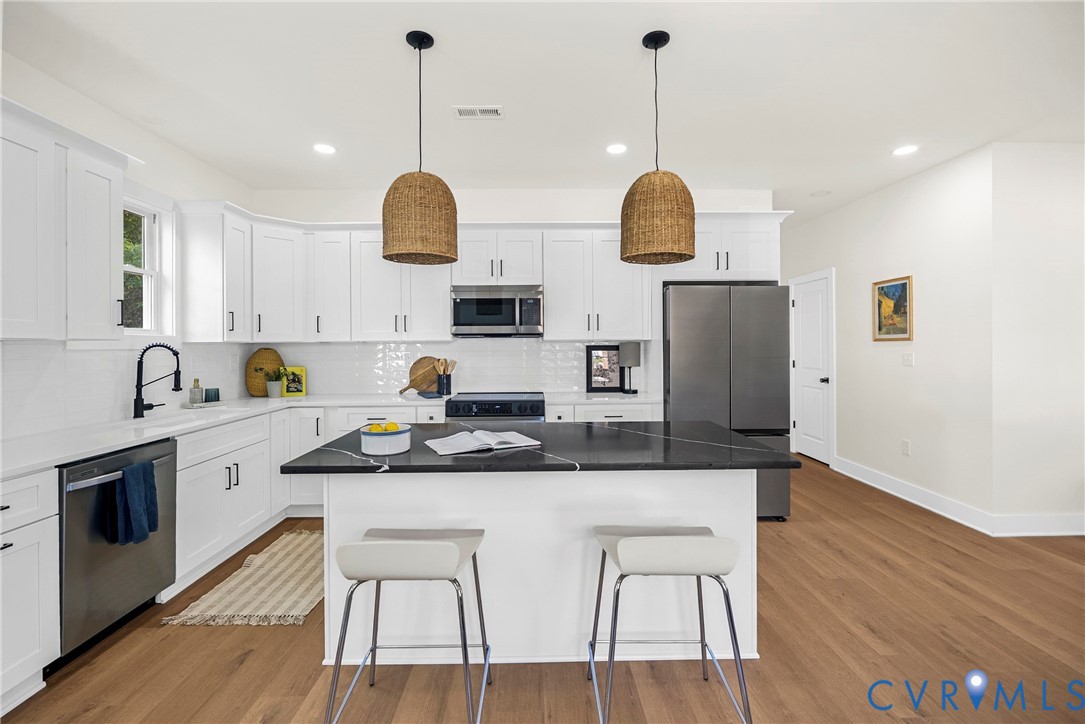 Kitchen featuring white shaker-style cabinetry, a central island with a dark stone countertop, stainless steel appliances, white subway tile backsplash, and wood-finish flooring