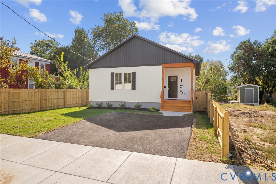 Exterior featuring vertical siding, a wood-framed covered entrance, asphalt driveway, and perimeter wood fencing