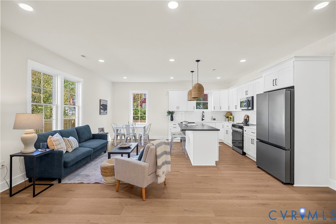 Open-concept kitchen featuring white shaker-style cabinetry, quartz countertops, an island with bar seating, and wood-finish flooring