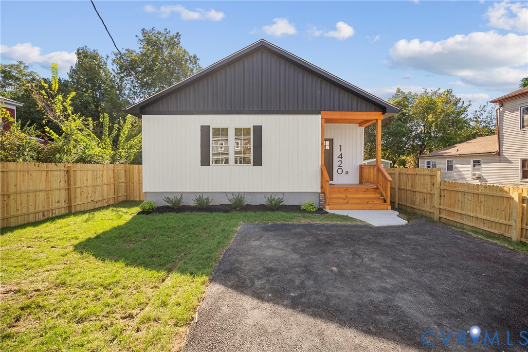 Exterior featuring vertical siding, a wood-frame covered porch, asphalt driveway, and wooden perimeter fencing