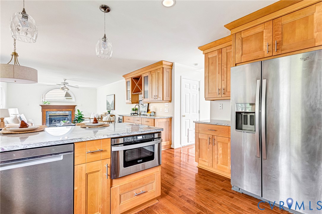 Kitchen featuring light wood cabinetry, stone countertops, stainless steel appliances including a built-in microwave, wood-finish flooring, and multi-pendant lighting