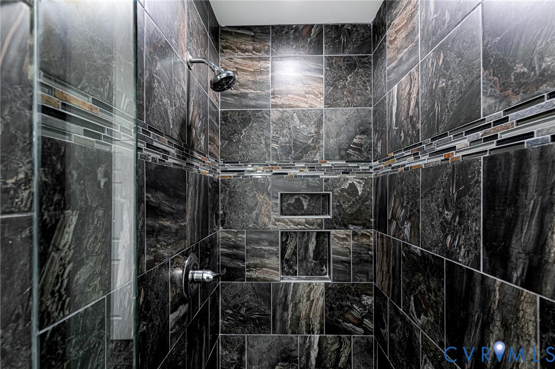 Walk-in shower featuring dark natural stone wall tile, decorative linear mosaic accent tile, integrated dual wall niches, and chrome fixtures