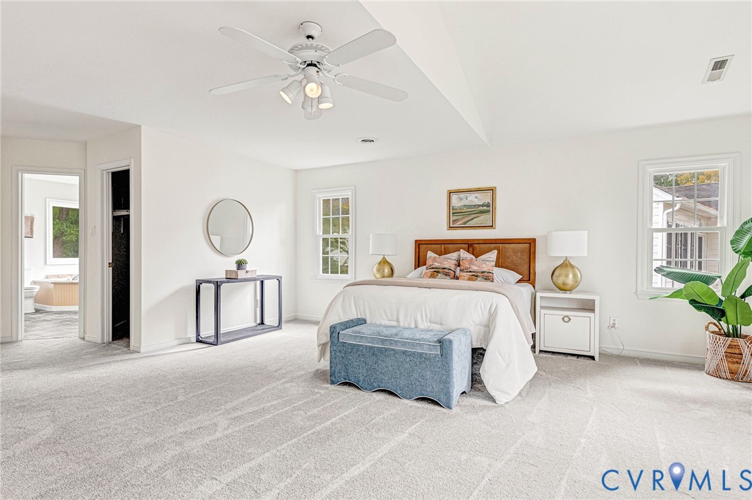 Spacious room featuring neutral carpeting, a white ceiling fan with integrated lighting, and multiple double-hung windows