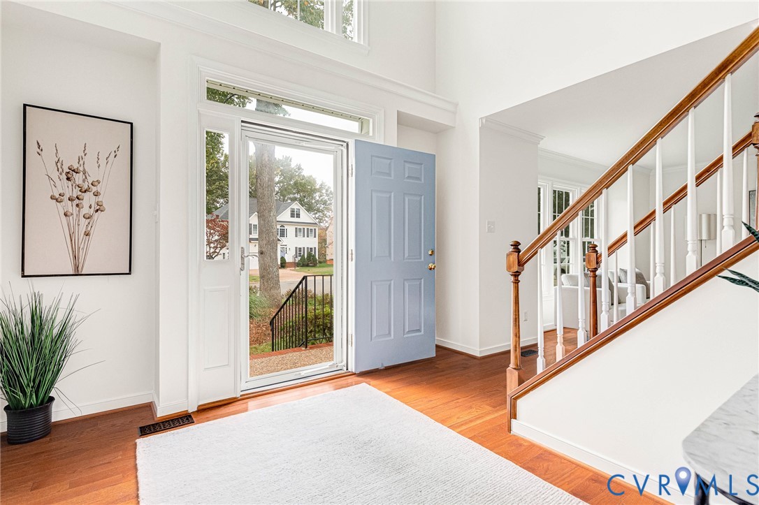 Foyer featuring soaring ceilings, wood-finish flooring, a wood-railing staircase, and a glass-paneled entry door with transom window Foyer featuring soaring ceilings, wood-finish flooring, a wood-railing staircase, and a glass-paneled entry door with transom window