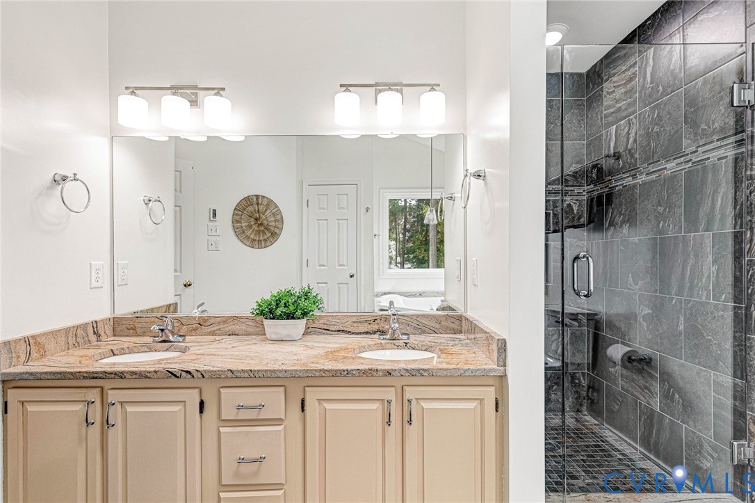 Double vanity with a stone countertop, dual drop-in sinks, integrated mirror, and a glass-enclosed shower featuring tile walls