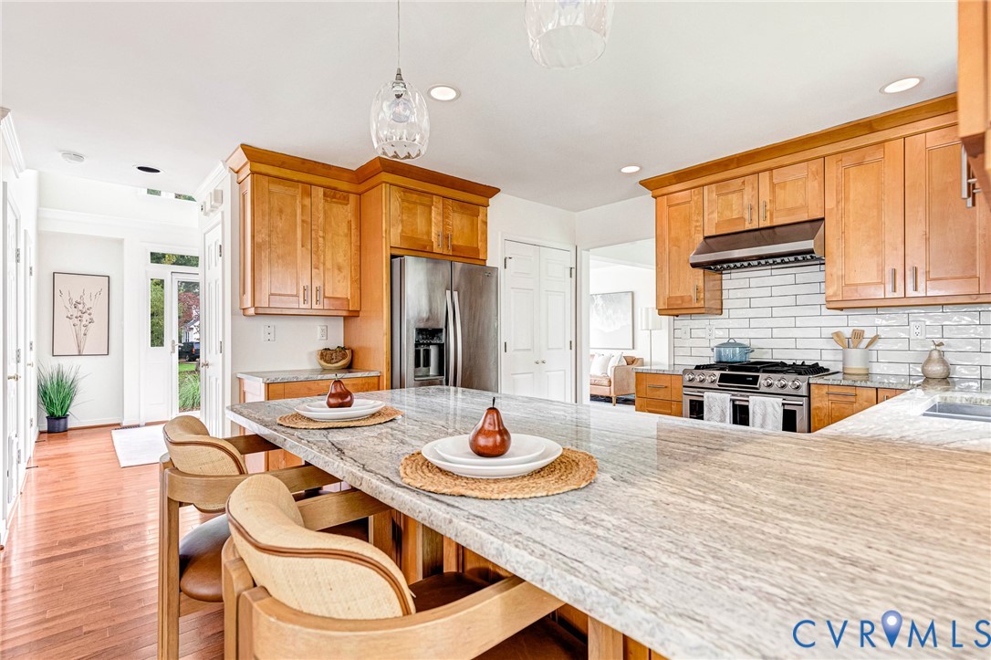 Kitchen featuring wood cabinetry, natural stone countertops, a central island, a tile backsplash, and stainless steel appliances