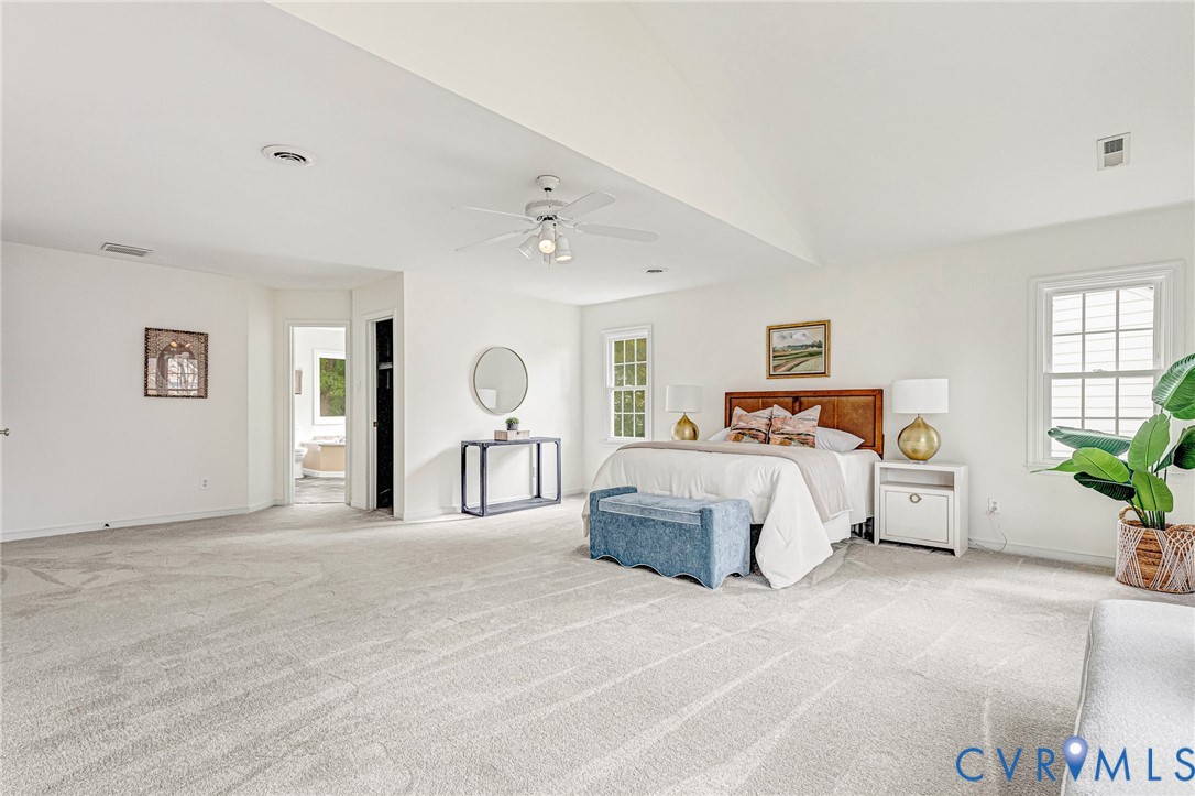 Spacious room featuring a vaulted ceiling, neutral wall-to-wall carpeting, multiple windows, and a ceiling fan with integrated lighting