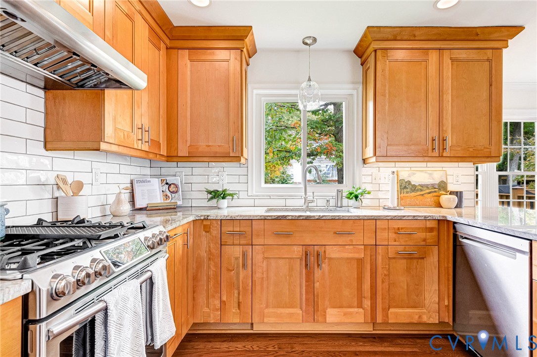 Kitchen featuring wood cabinetry, white subway tile backsplash, stone countertops, stainless steel gas range with overhead exhaust hood, and stainless steel dishwasher