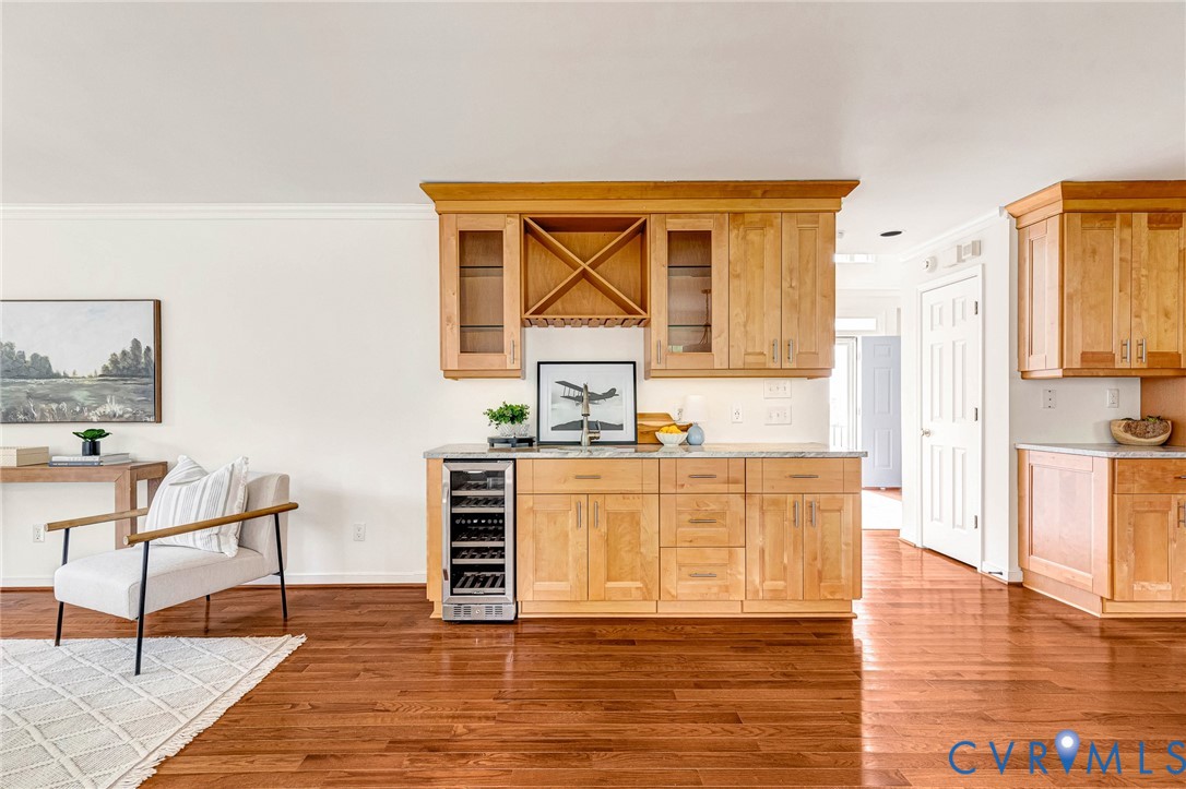 Built-in wet bar featuring natural wood cabinetry, glass-paneled upper cabinets, integrated wine storage, and a stainless steel under-counter wine refrigerator, complemented by wood-finish flooring