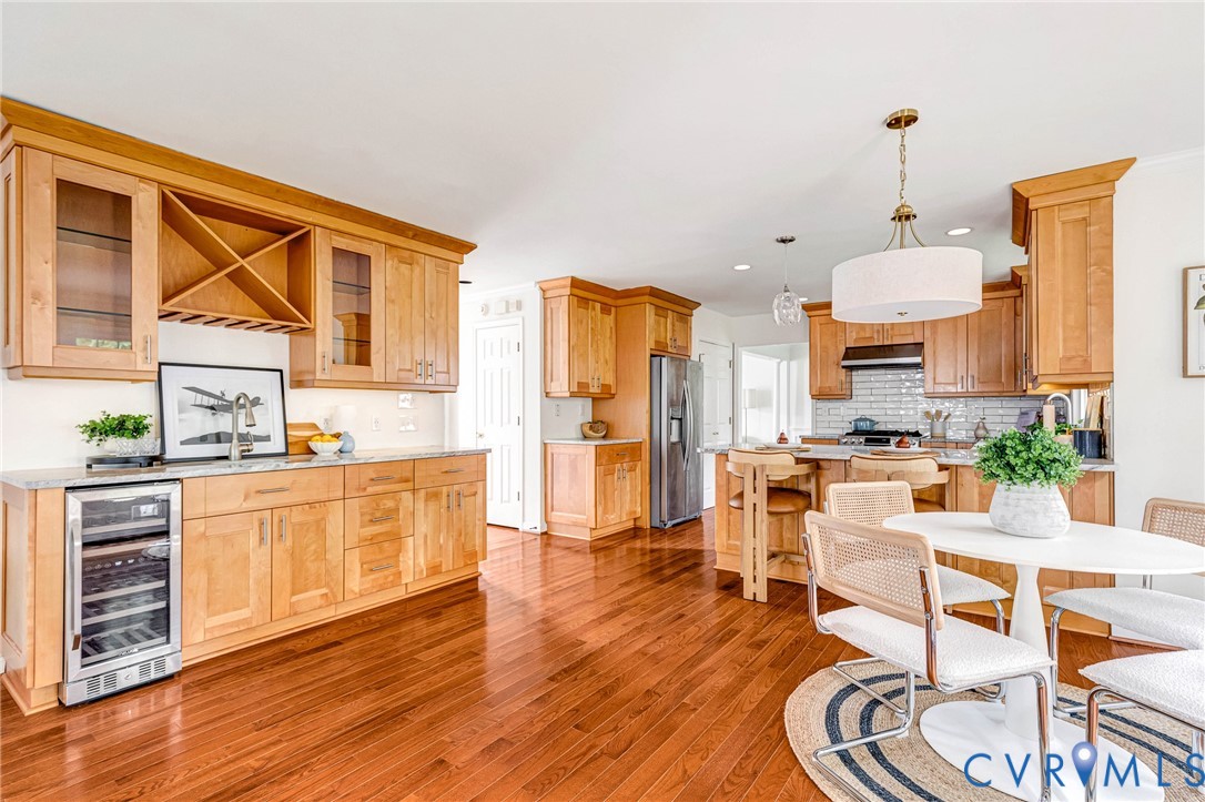 Kitchen featuring natural wood cabinetry, built-in wine cooler, stone countertops, subway tile backsplash, and wood-finish flooring