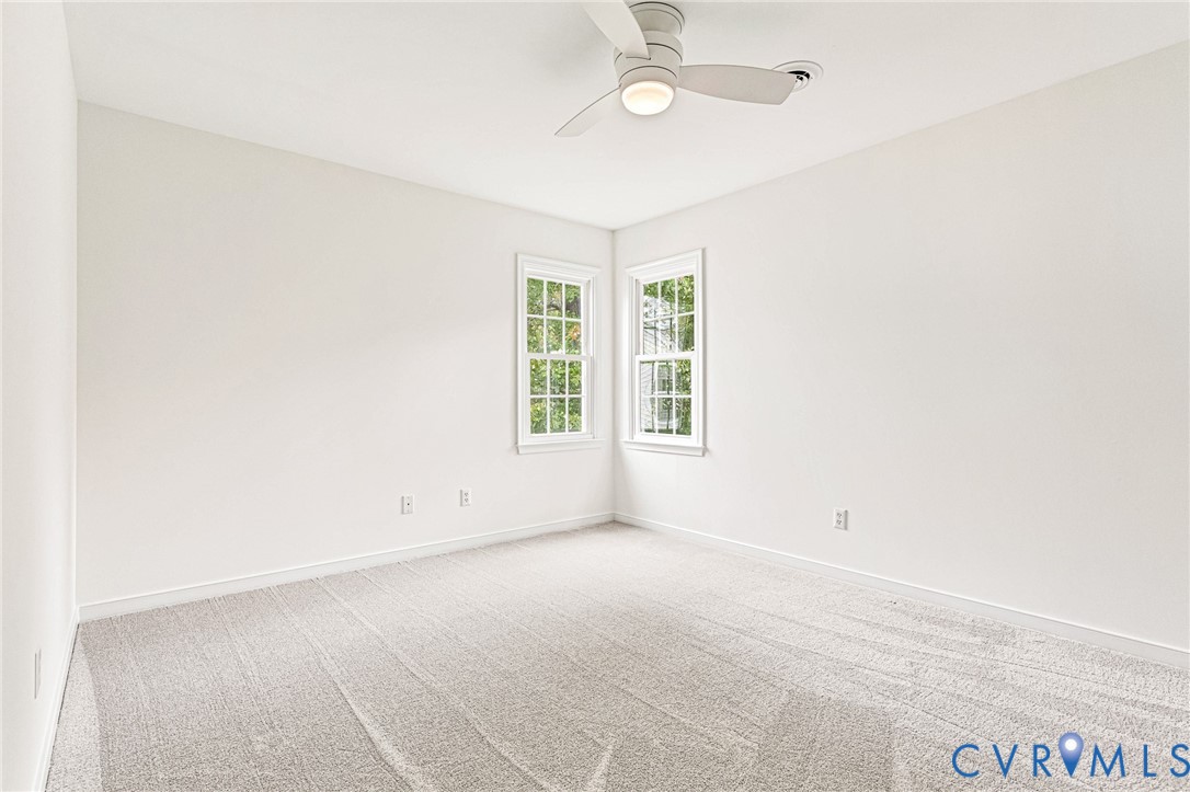 Neutral-toned interior featuring wall-to-wall carpeting, dual double-hung windows, and a flush-mount ceiling fan with integrated lighting