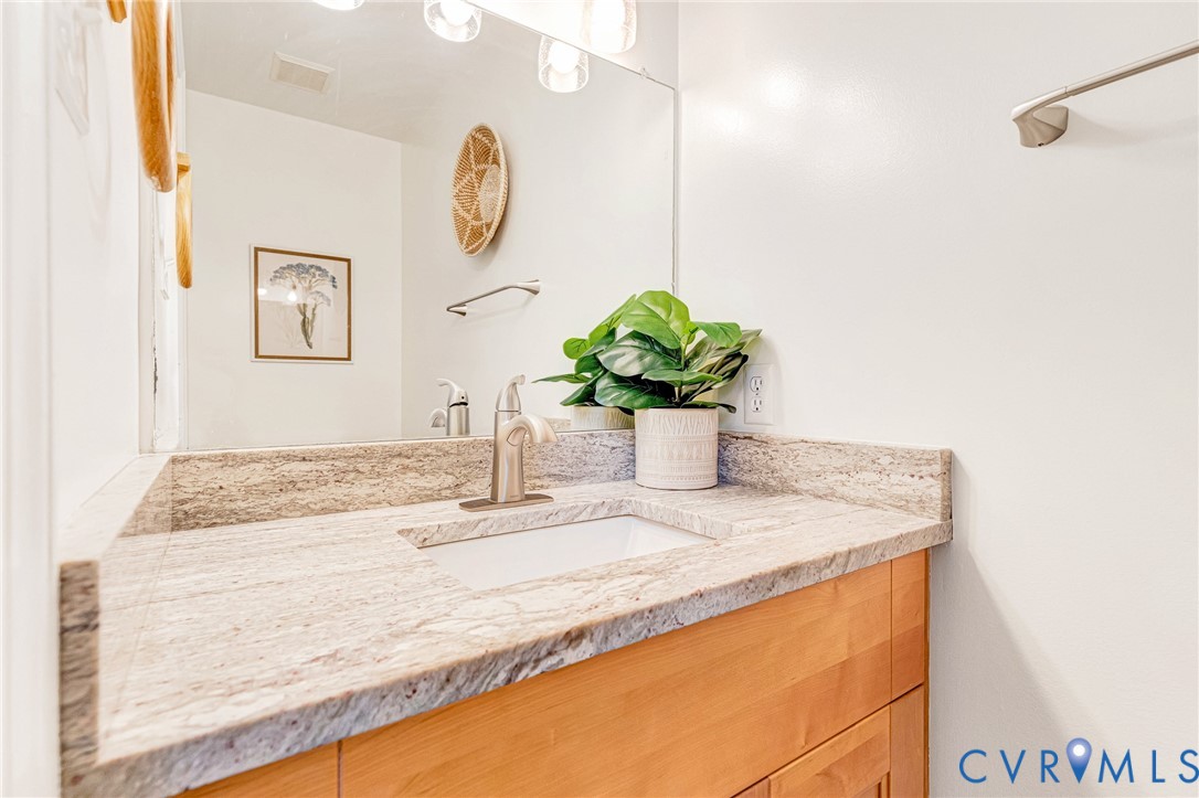 Vanity featuring a stone-surface countertop, an integrated rectangular undermount sink, a brushed-metal single-handle faucet, light-finish wooden cabinetry, and a full-width wall-mounted mirror