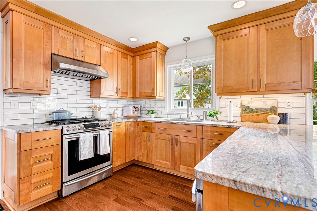 Kitchen featuring light-finish cabinetry, stone countertops, white subway tile backsplash, stainless steel gas range with overhead vent hood, and wood-finish flooring