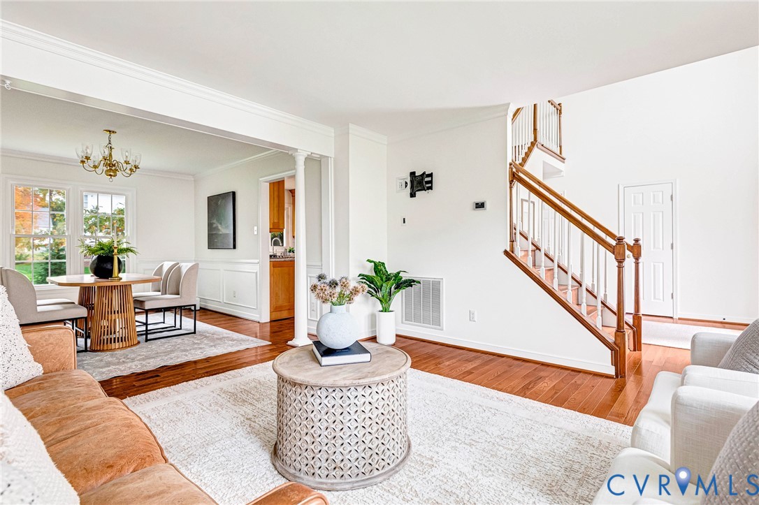 Interior featuring wood-finish flooring, a traditional staircase with a wooden handrail, wainscoting detail, crown molding, and a built-in column Interior featuring wood-finish flooring, a traditional staircase with a wooden handrail, wainscoting detail, crown molding, and a built-in column