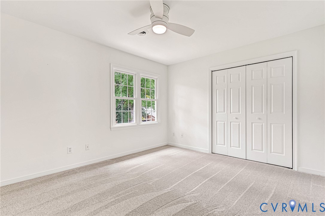 Neutral carpet flooring, multi-panel closet doors, white ceiling fan with integrated lighting, and dual-pane windows with grid mullions