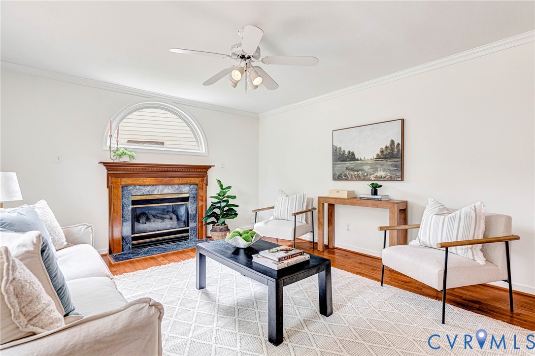 Fireplace featuring a decorative wood mantel, stone surround, and an arched transom window above, complemented by wood-finish flooring and a central ceiling fan with integrated lighting
