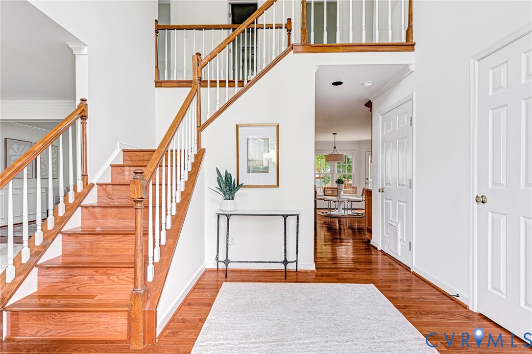 Foyer featuring wood-finish flooring, a wooden staircase with white balusters, and crown molding Foyer featuring wood-finish flooring, a wooden staircase with white balusters, and crown molding
