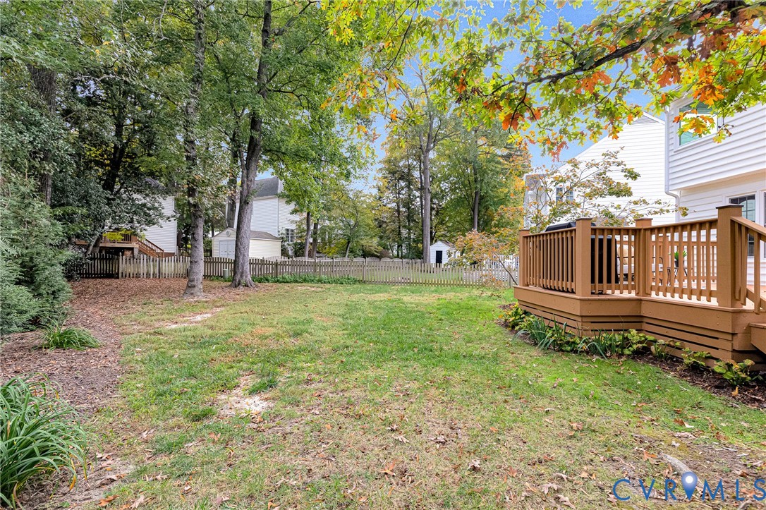 Backyard featuring a raised wooden deck, white horizontal siding, perimeter picket fencing, and mature trees