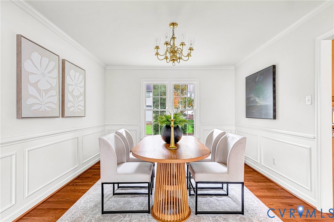 Dining area featuring classic crown molding, wainscoting, wood-finish flooring, multi-pane windows, and a traditional chandelier Dining area featuring classic crown molding, wainscoting, wood-finish flooring, multi-pane windows, and a traditional chandelier