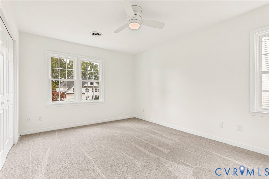Neutral interior featuring neutral carpeting, crisp white wall finishes, multi-pane windows, and a central ceiling fan with an integrated light fixture
