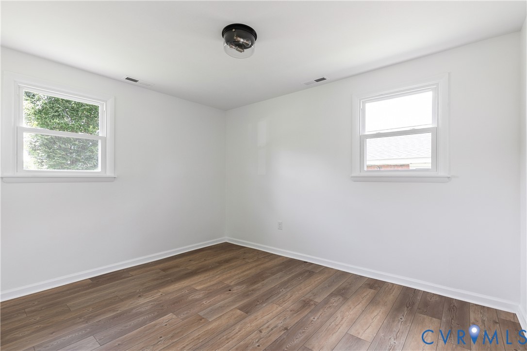 Interior space featuring wood-finish flooring, white walls, dual windows, and a central flush-mount ceiling fixture