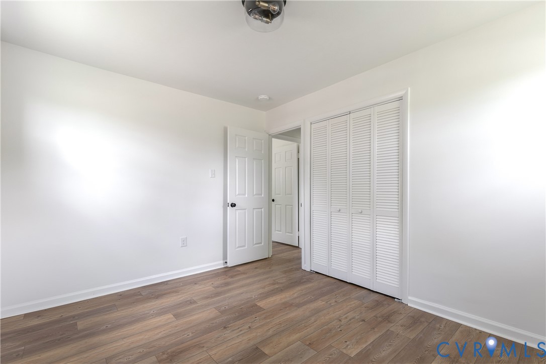 Room featuring wood-finish flooring, white walls, louvered bi-fold closet doors, and a flush-mount ceiling light fixture
