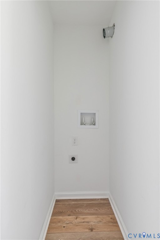 Utility area featuring wood-finish flooring, a recessed water supply box, integrated electrical outlets, and a wall-mounted dryer vent connection