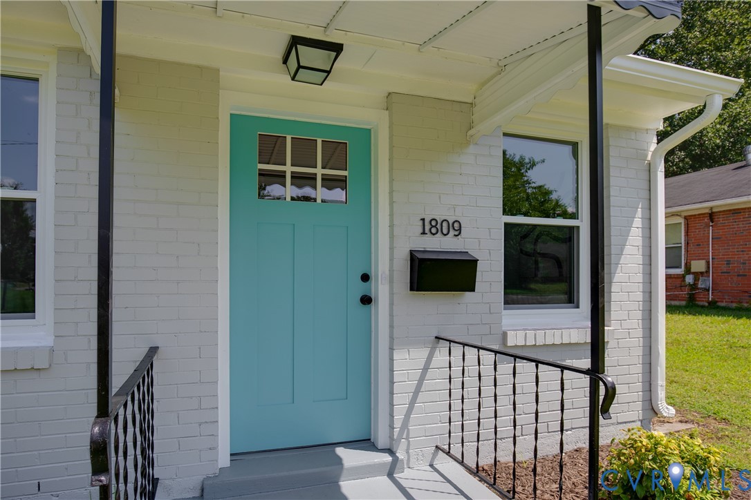 Painted brick exterior featuring a teal-accented front door with glass insert, black wrought-iron porch railings, and a geometric flush-mount light fixture