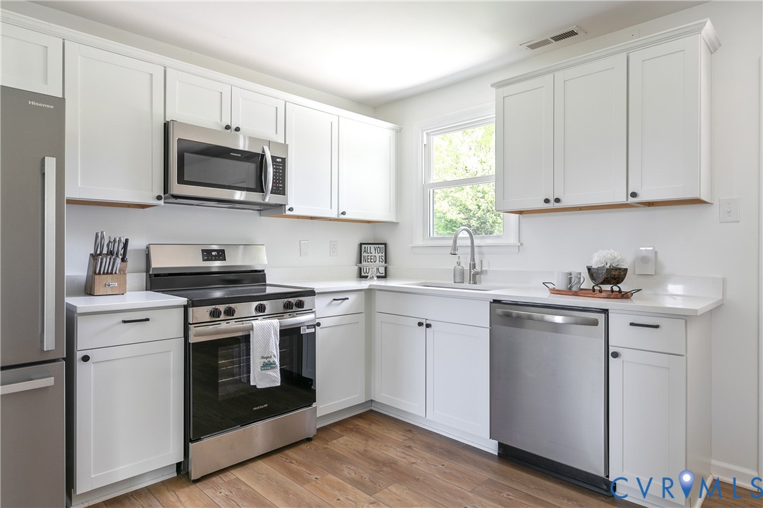 Kitchen featuring white shaker-style cabinetry, solid-surface countertops, wood-finish flooring, and stainless steel appliances