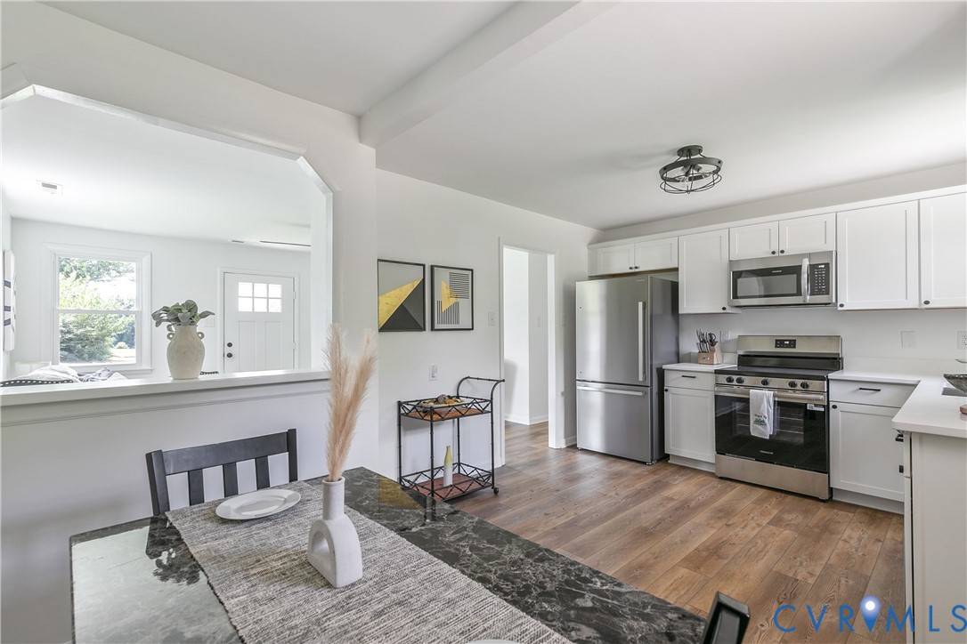 Kitchen featuring white cabinetry, stainless steel appliances, wood-finish flooring, and a pass-through opening